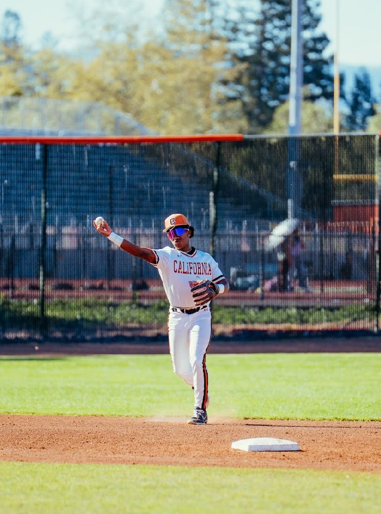 Kai Watts making a throw from the middle infield next to second base, in the white California home uniform
